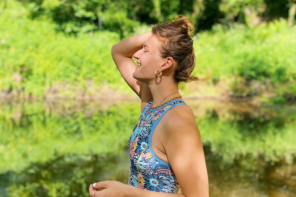 Happy girl stands by river amongst green foliage in a swimsuit