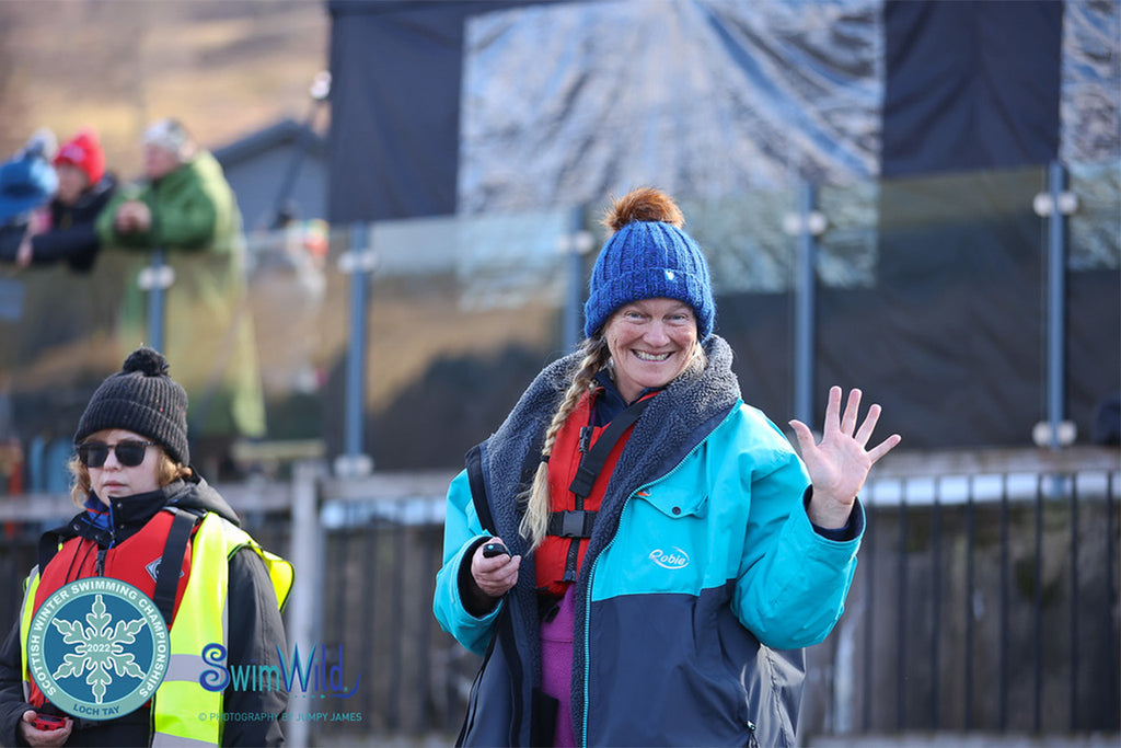 Sara waves at the camera wearing a Robie and blue bobble hat