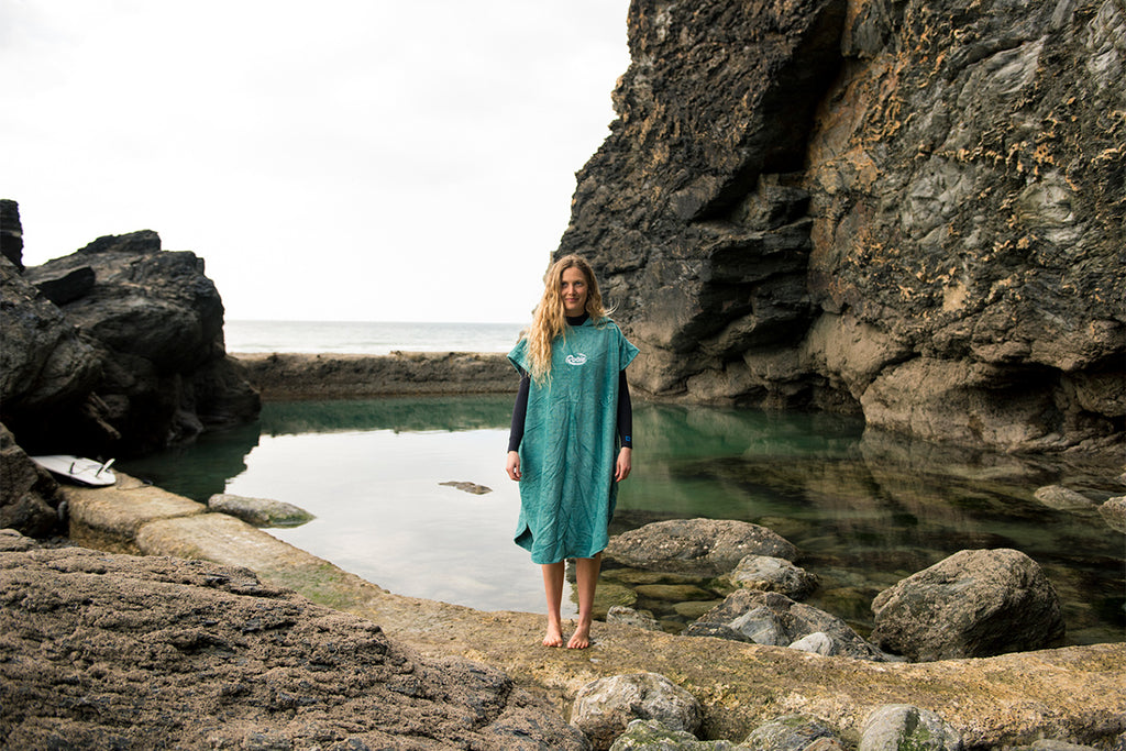 woman standings wearing green towelling robe on the edge of a sea pool