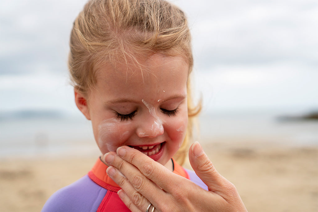blonde child has suncream wiped on her face by parent