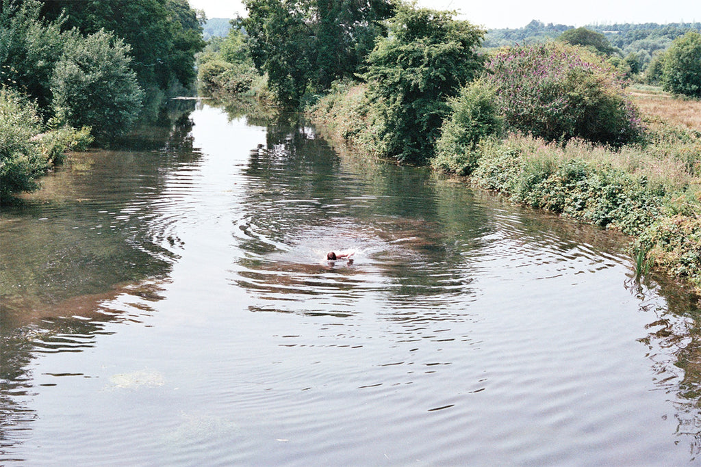 man swimming in river surrounded by trees and fields